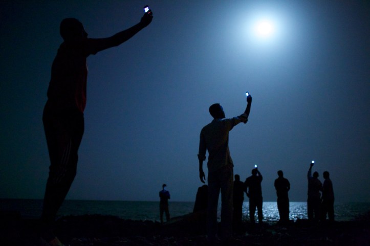 World Press Photo of the Year 2013: 26 February 2013, Djibouti City, Djibouti African migrants on the shore of Djibouti city at night, raising their phones in an attempt to capture an inexpensive signal from neighbouring Somalia—a tenuous link to relatives abroad. Djibouti is a common stop-off point for migrants in transit from such countries as Somalia, Ethiopia and Eritrea, seeking a better life in Europe and the Middle East © John Stanmeyer, USA, VII for National Geographic